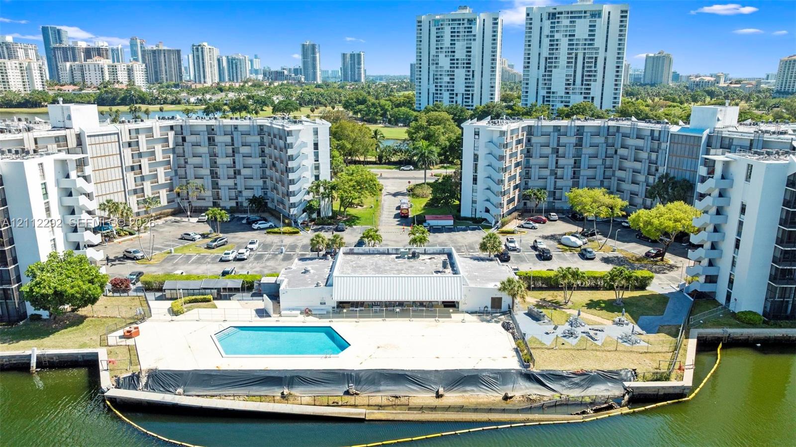 Waterfront multi-story residential complex featuring an outdoor swimming pool, paved surface parking, and manicured perimeter landscaping Waterfront multi-story residential complex featuring an outdoor swimming pool, paved surface parking, and manicured perimeter landscaping