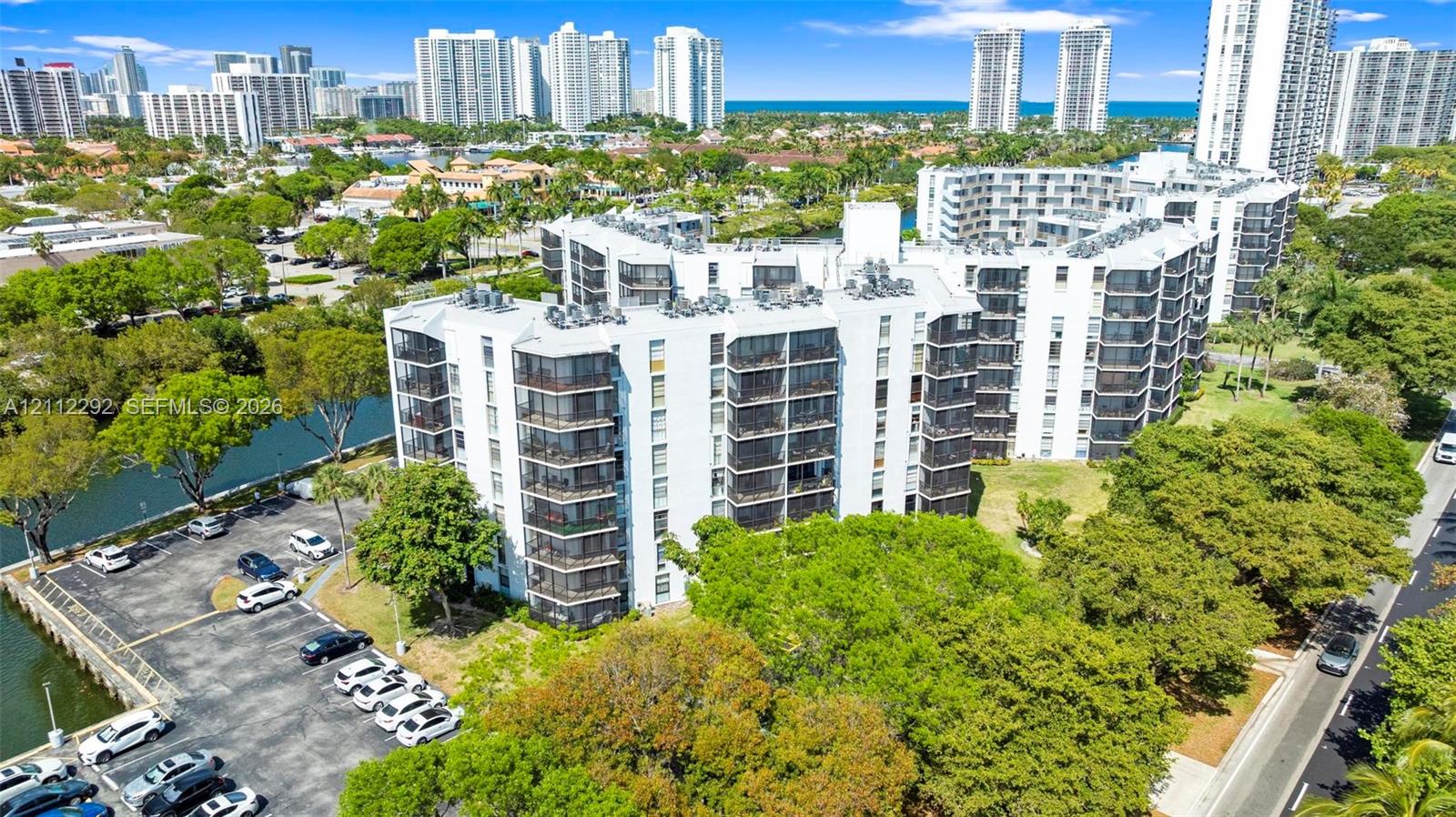 Multi-story building featuring screened balconies, water-adjacent hardscaping, paved parking, and landscaped grounds Multi-story building featuring screened balconies, water-adjacent hardscaping, paved parking, and landscaped grounds