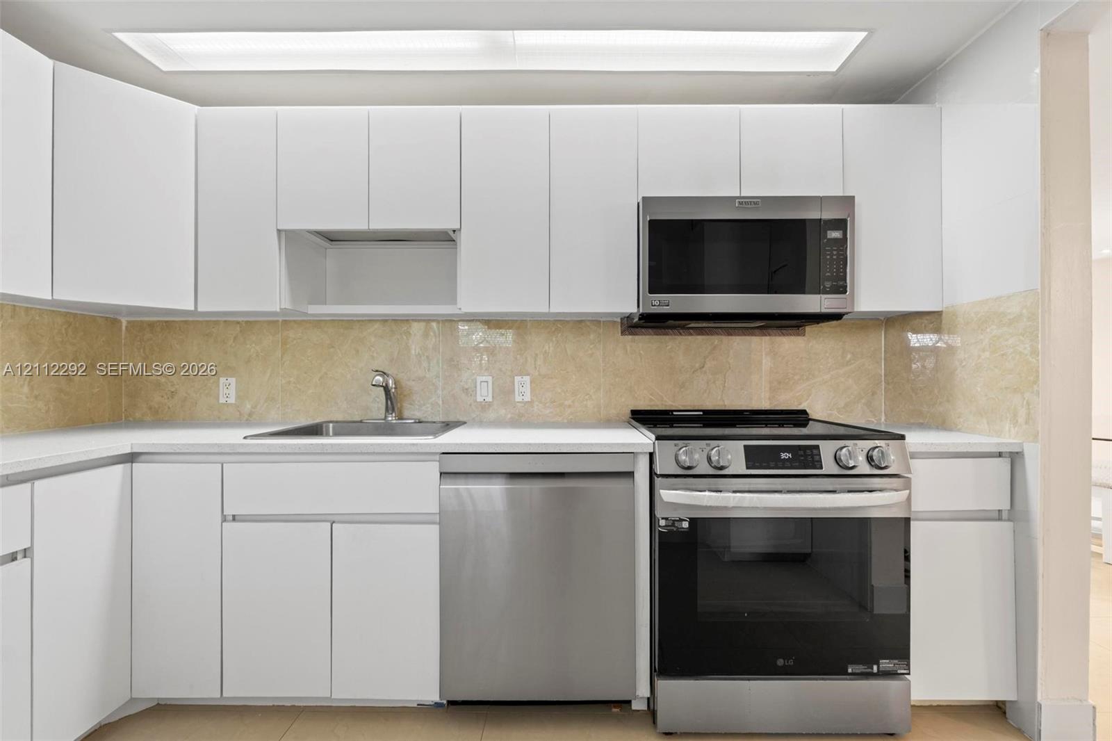 Kitchen featuring white flat-panel cabinetry, stone-finish backsplash, stainless steel appliances, solid-surface countertops, and recessed lighting