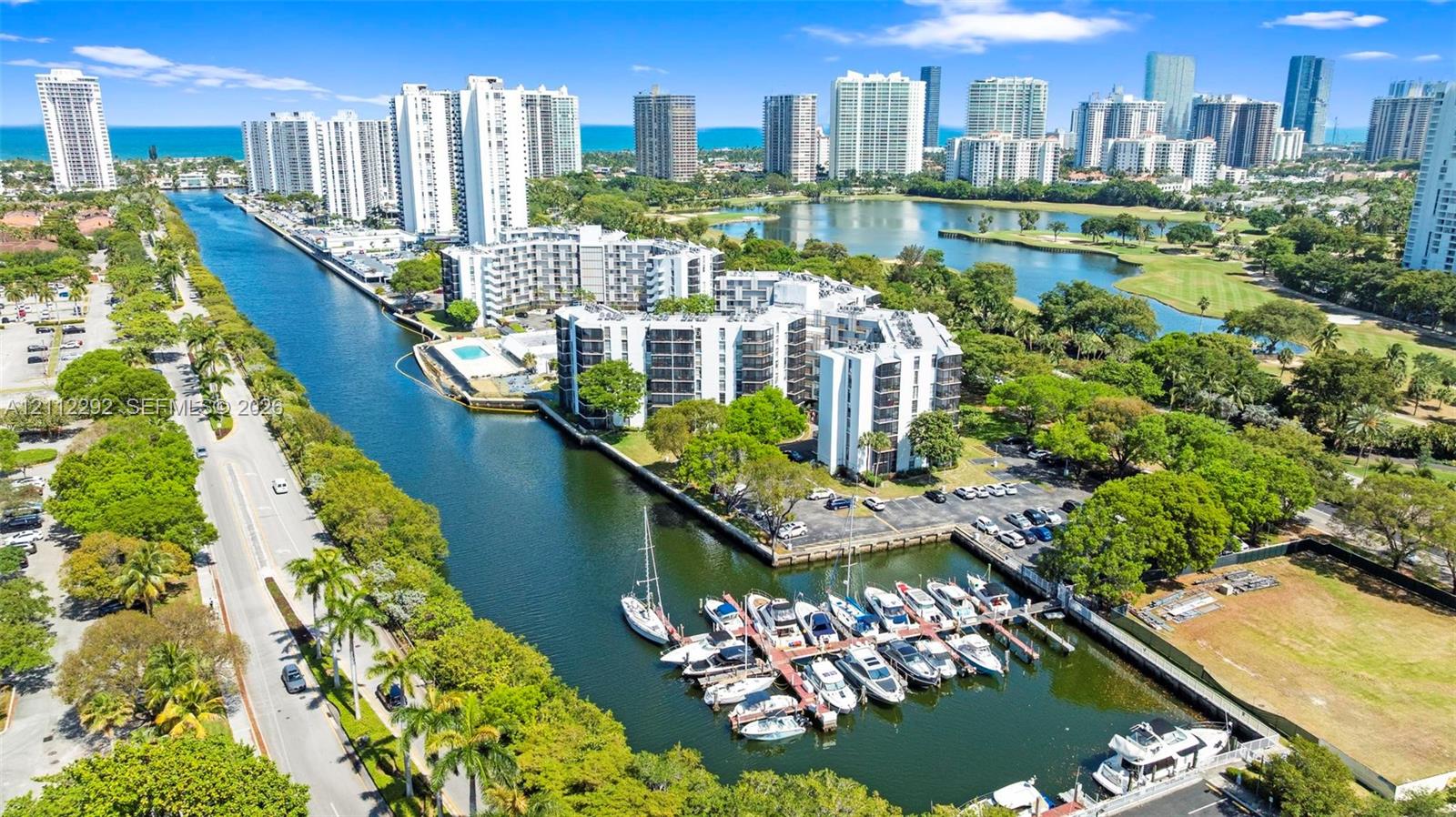 Aerial perspective of waterfront mid-rise buildings featuring a private deep-water dock, integrated boat slips, paved parking areas, and mature landscape elements Aerial perspective of waterfront mid-rise buildings featuring a private deep-water dock, integrated boat slips, paved parking areas, and mature landscape elements