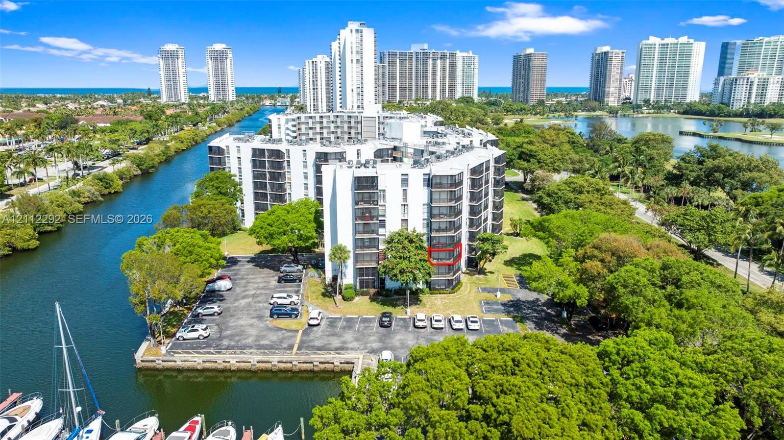 Multi-story waterfront condominium building featuring exterior balconies, paved surface parking, and a bulkhead-lined canal with boat slips Multi-story waterfront condominium building featuring exterior balconies, paved surface parking, and a bulkhead-lined canal with boat slips