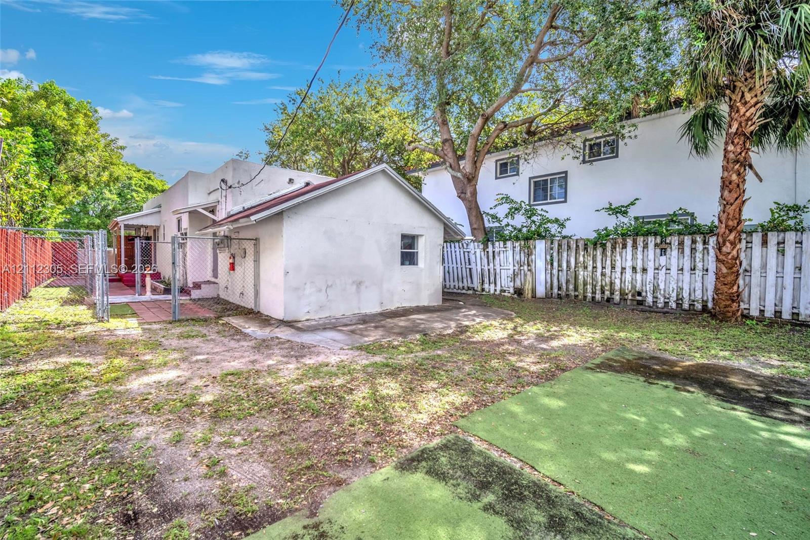 Exterior space featuring a detached building, paved brick patio area, chain-link and wood perimeter fencing, and mature trees