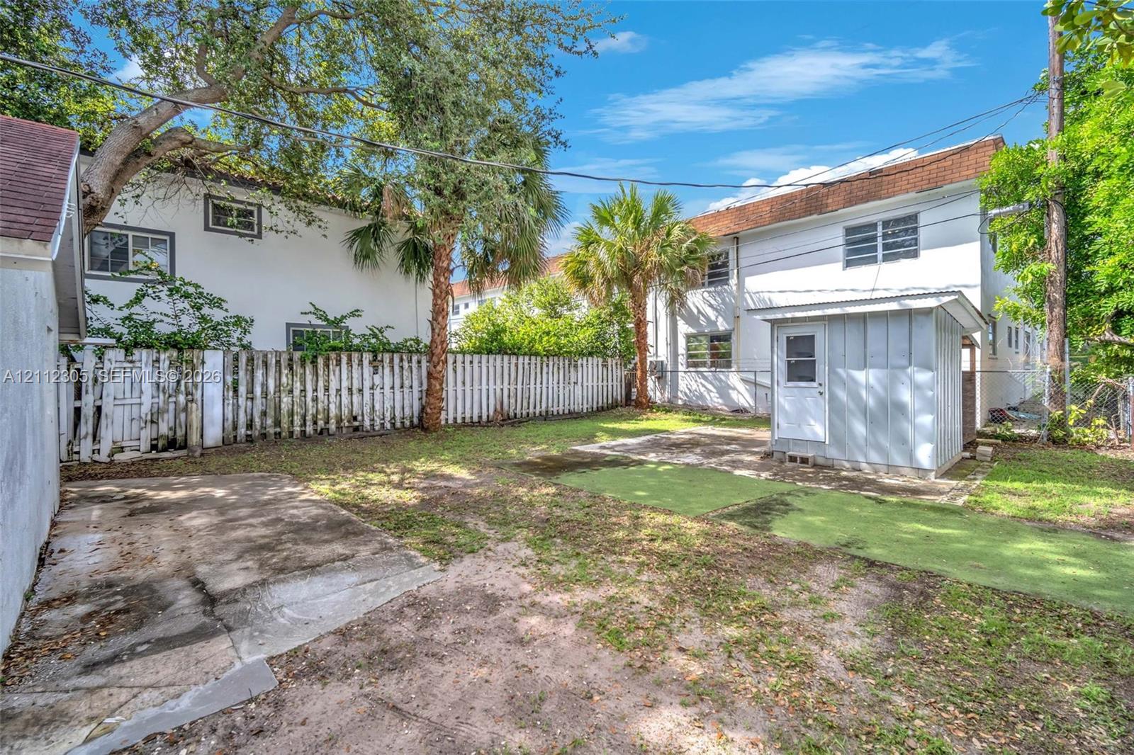 Rear exterior featuring a detached structure, concrete patio, artificial turf area, and full-perimeter wood fencing