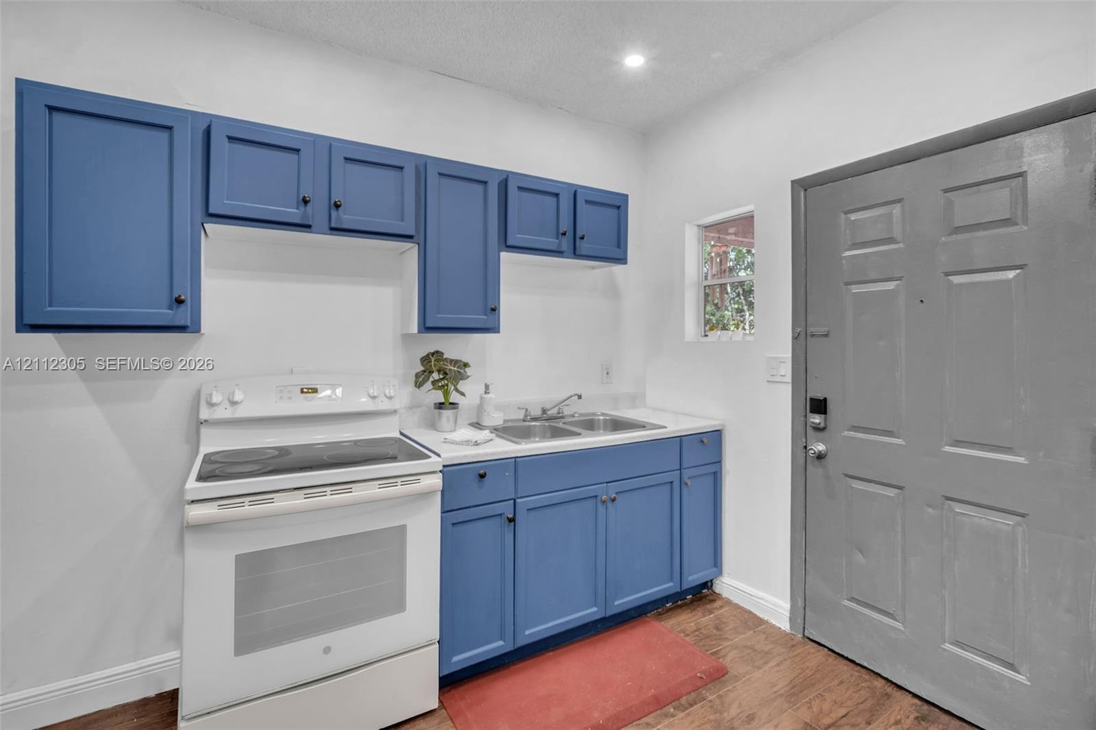Blue cabinetry with shaker-style doors, white electric range, double-basin stainless steel sink, solid-surface countertop, and wood-finish flooring