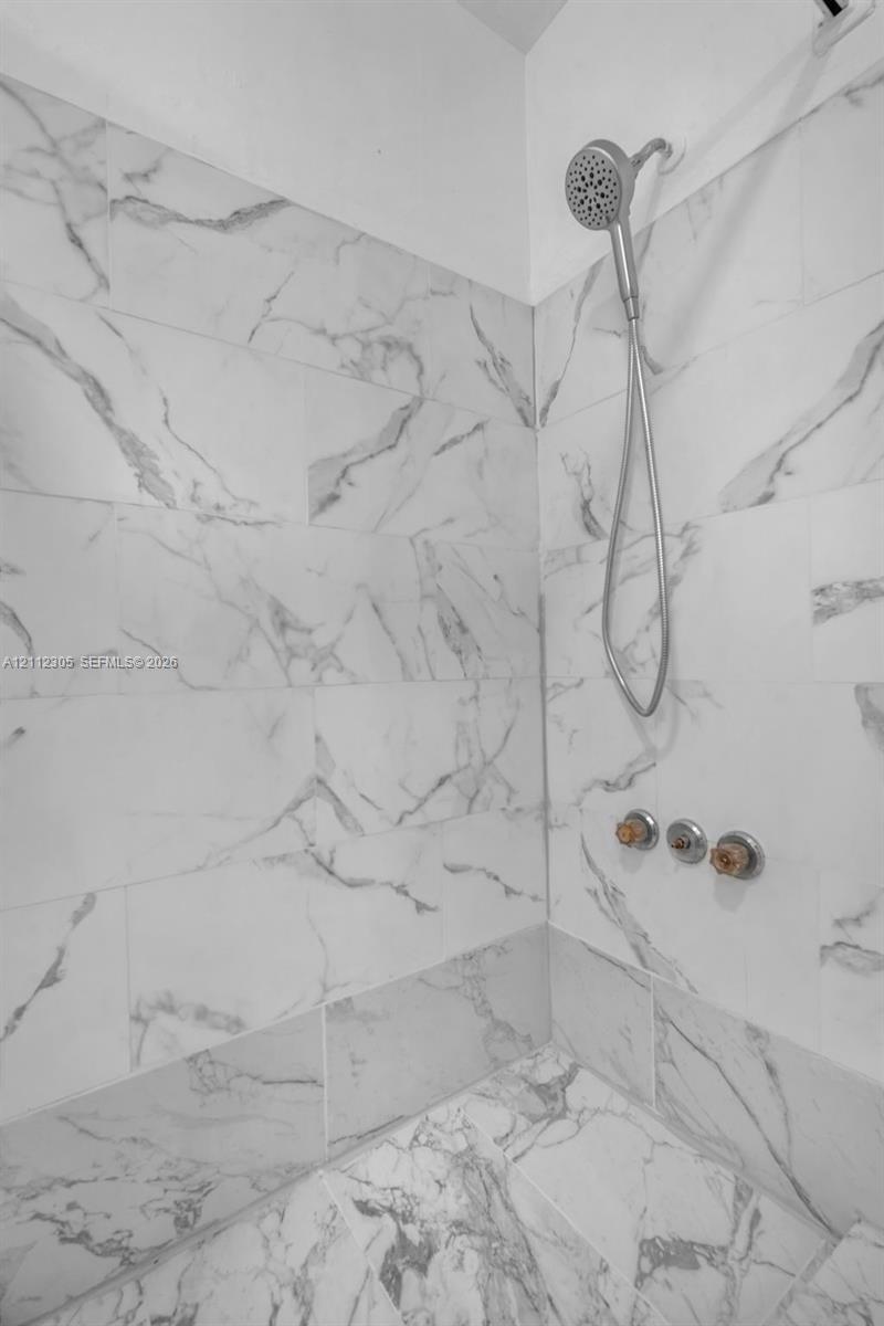 Shower enclosure featuring large-format veined tile surround, metallic handheld shower fixture, and circular multi-handle valve controls