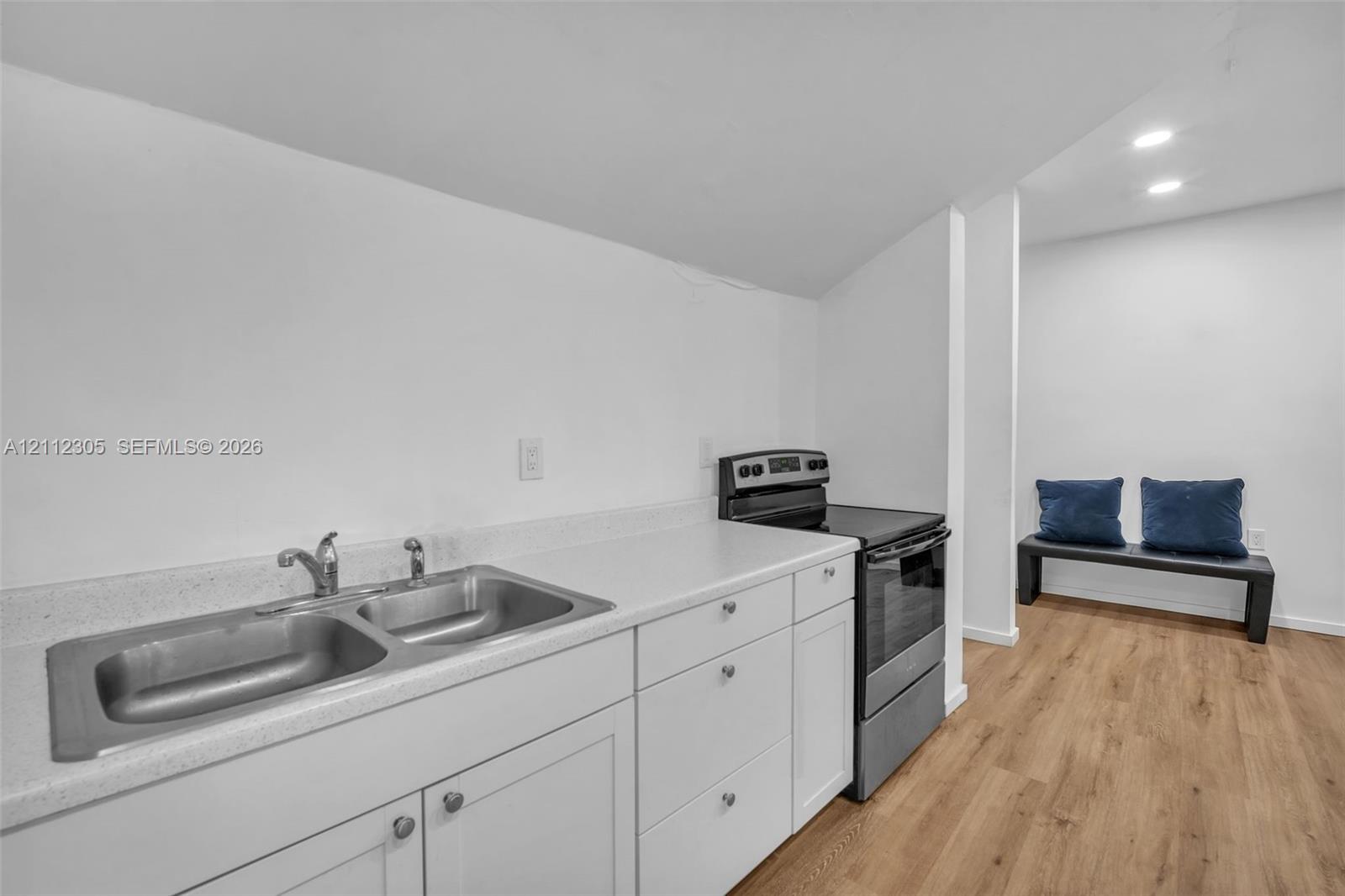 Kitchen area featuring white cabinetry, solid-surface countertops, dual-basin stainless steel sink, and wood-finish flooring