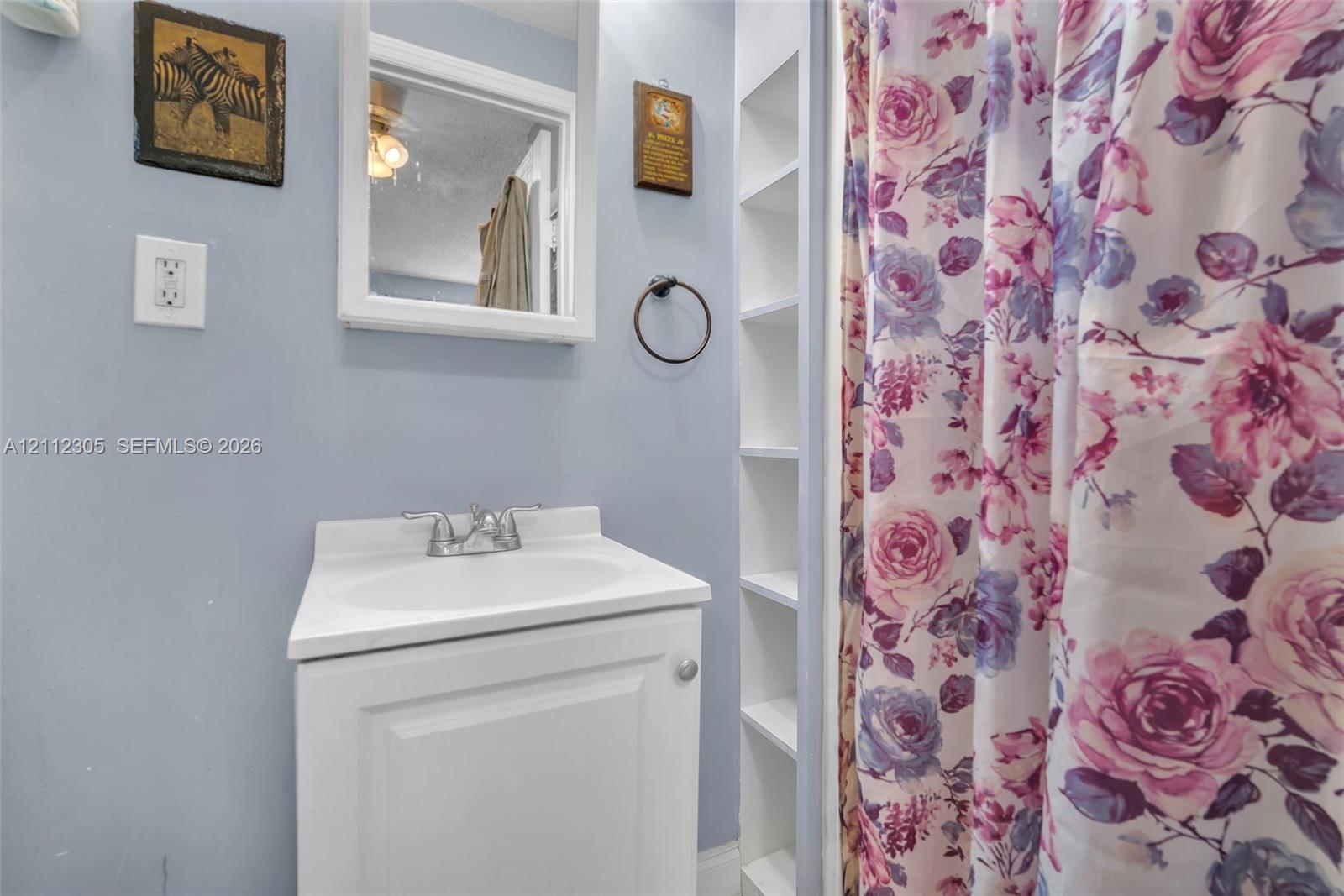 White vanity with integrated sink, chrome double-handle faucet, wall-mounted mirror, and built-in recessed shelving