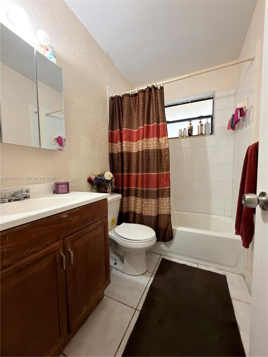Full bathroom featuring a wood-finish vanity with an integrated sink, a mirrored medicine cabinet, and a tub-shower combination with white wall tile