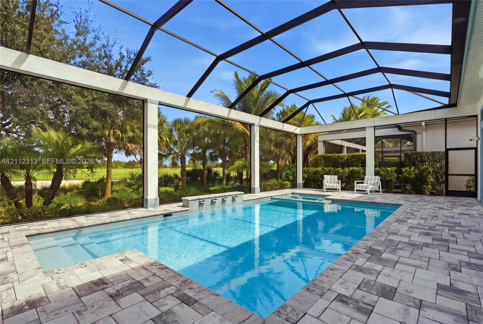 Screened pool enclosure featuring a stone-paver deck, built-in spa, and a wall fountain with multiple spillway spouts