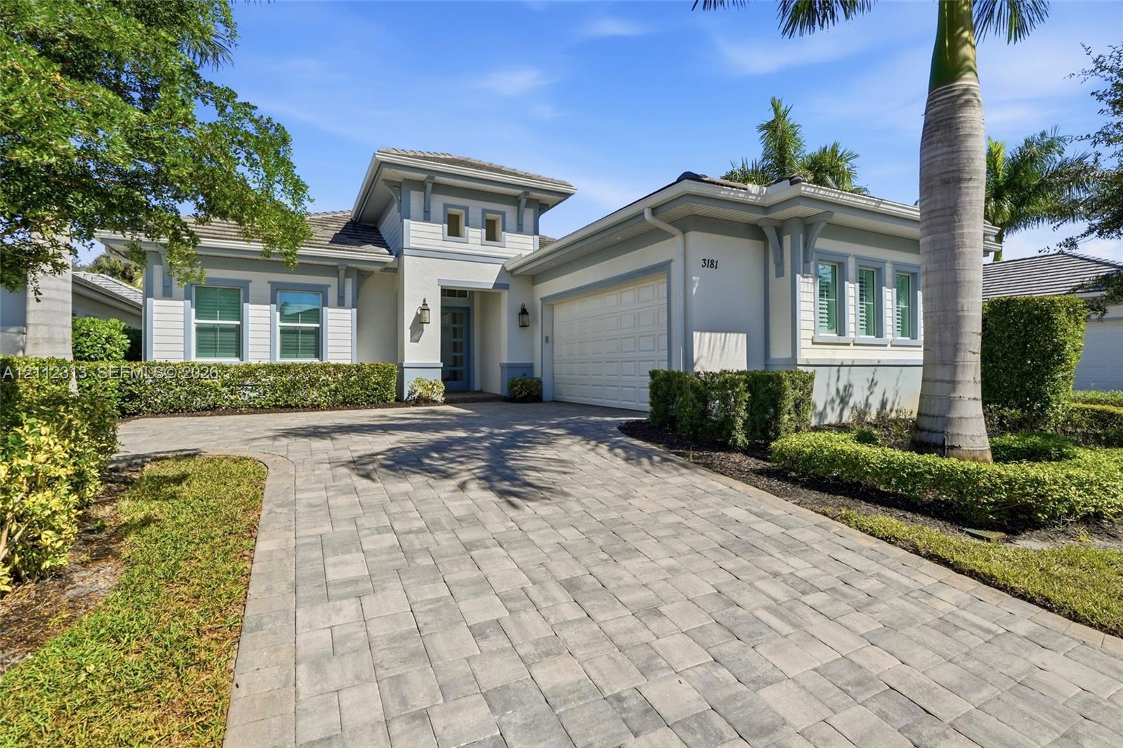 Single-story residence featuring a neutral stucco exterior, paver driveway, multi-pane windows, and a multi-tiered roofline with decorative corbels