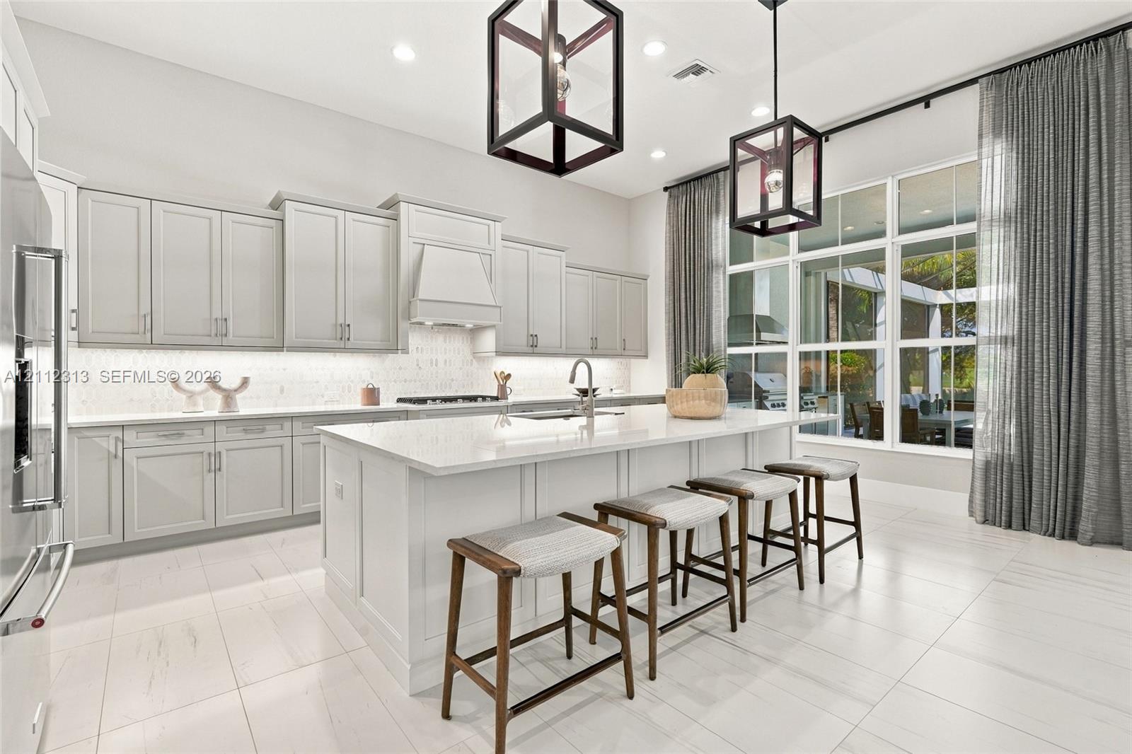 Kitchen featuring light-toned cabinetry, a large central island with a solid surface countertop, tile flooring, recessed lighting, and geometric pendant fixtures
