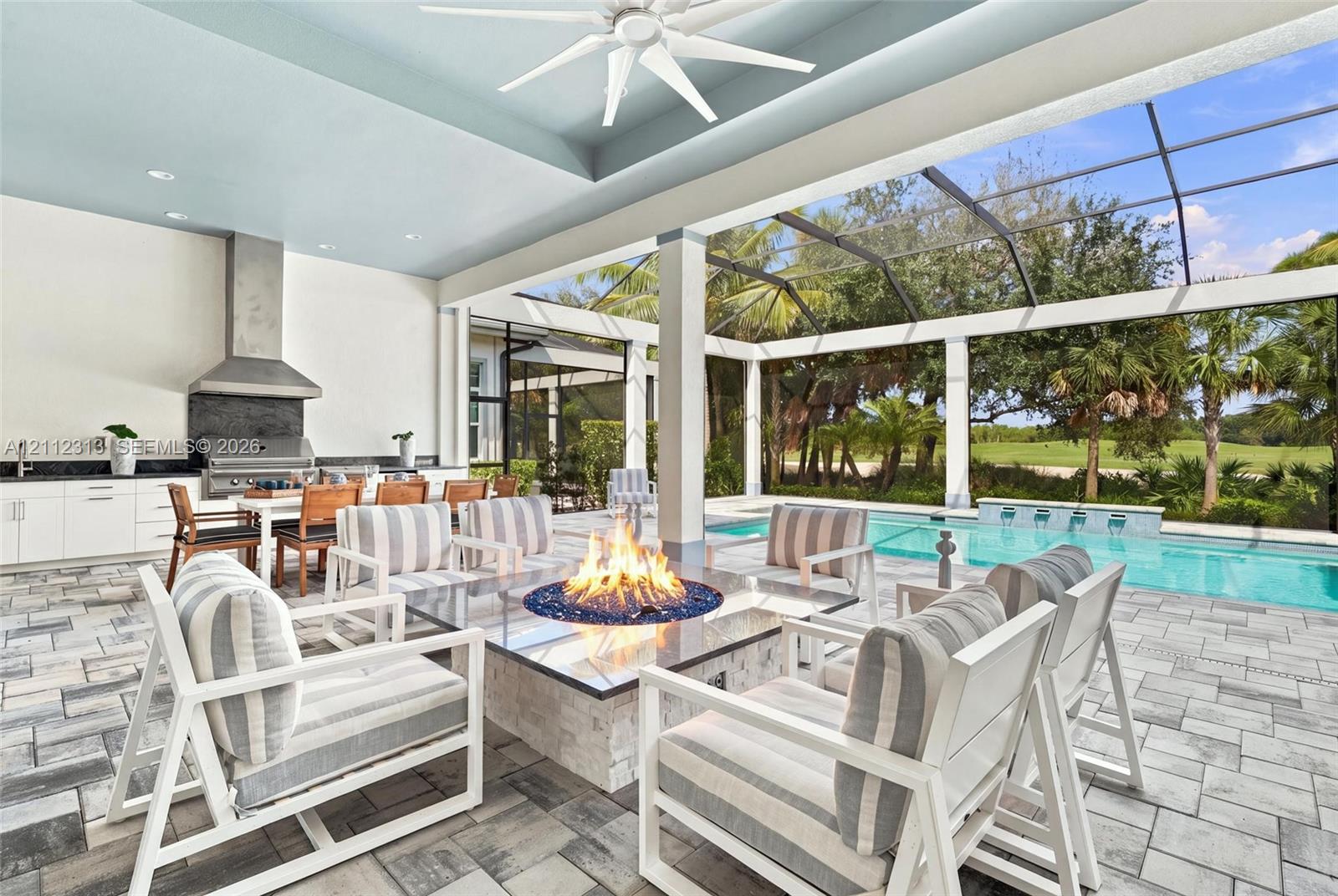 Covered outdoor living area featuring a built-in kitchen with stainless steel range hood, stone-clad fire feature, paver flooring, and a screened-in swimming pool