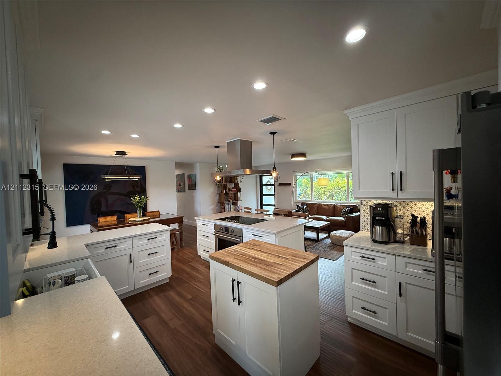 Kitchen featuring white cabinetry, light-toned stone-surface countertops, a mobile island with a wood-finish butcher block top, recessed lighting, and stainless steel appliances including an overhead range hood