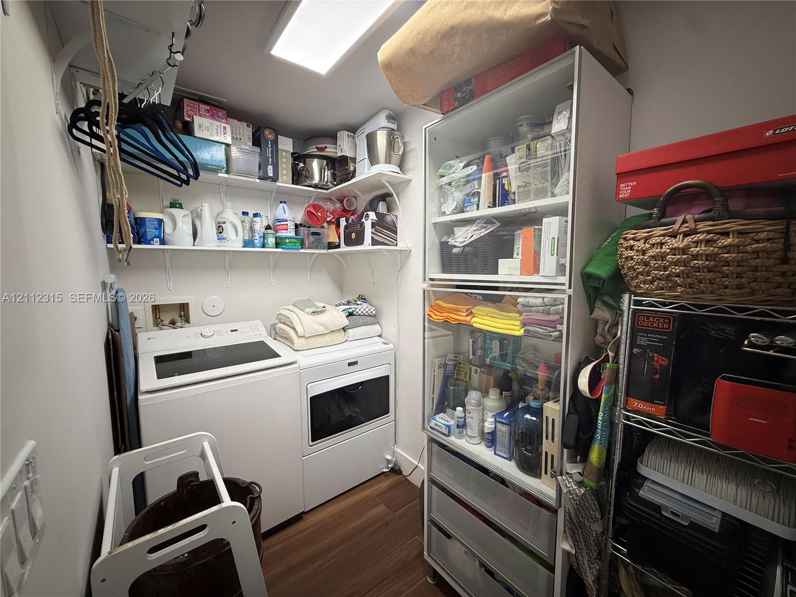 Laundry space featuring wood-finish flooring, white wall-mounted storage shelving, and built-in ceiling lighting