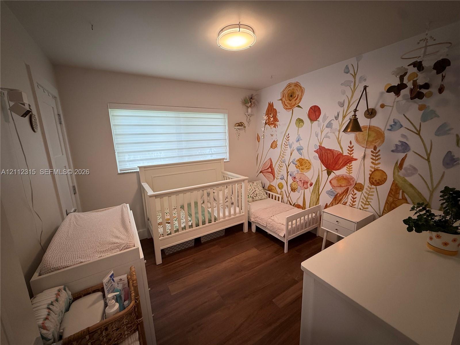 Wood-finish flooring, horizontal window blinds, wall-mounted adjustable metal light fixture, and decorative floral wall mural