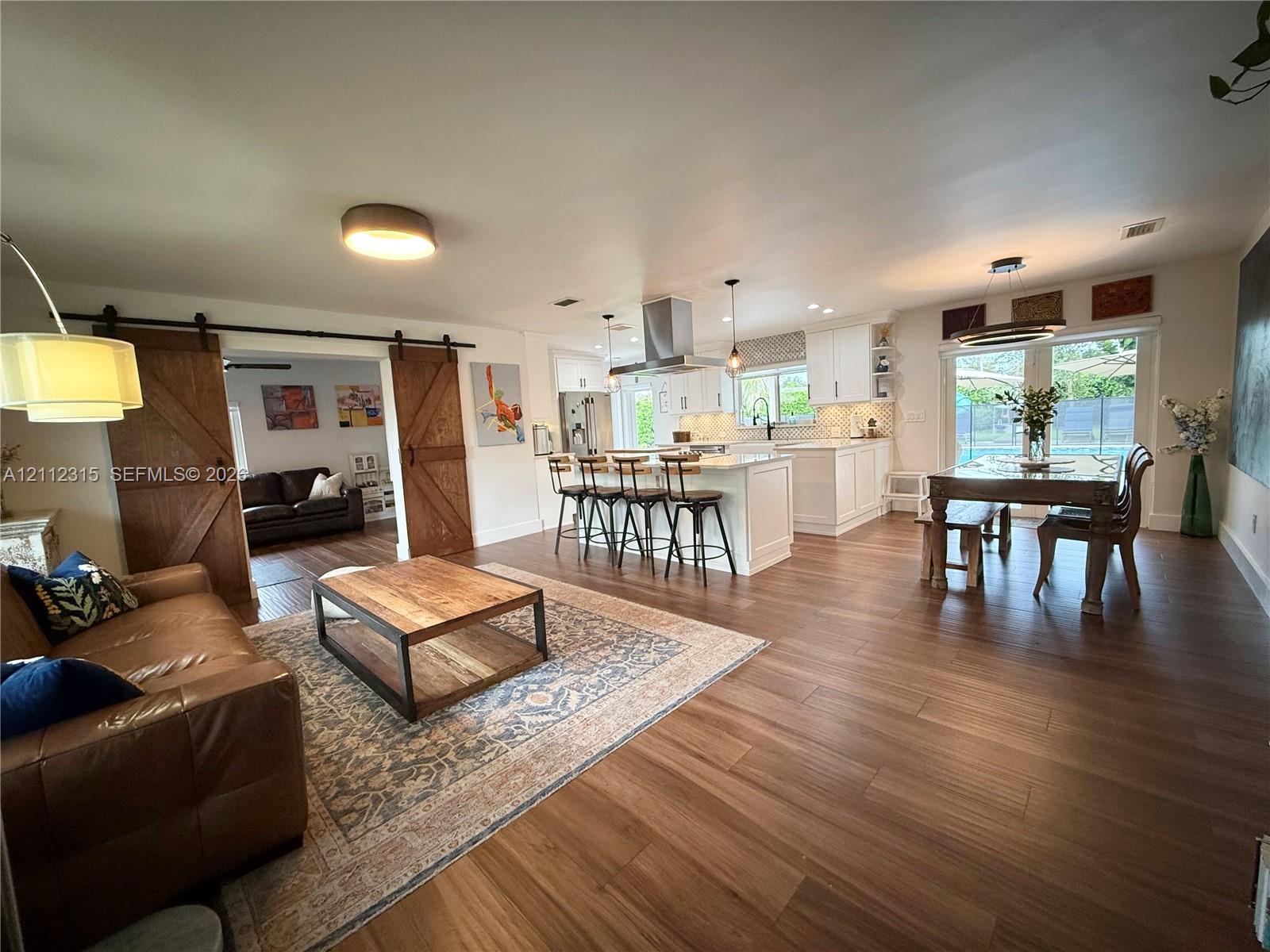 Open-concept interior featuring wood-finish flooring, a kitchen island with bar seating, a stainless steel range hood, and dual sliding barn doors