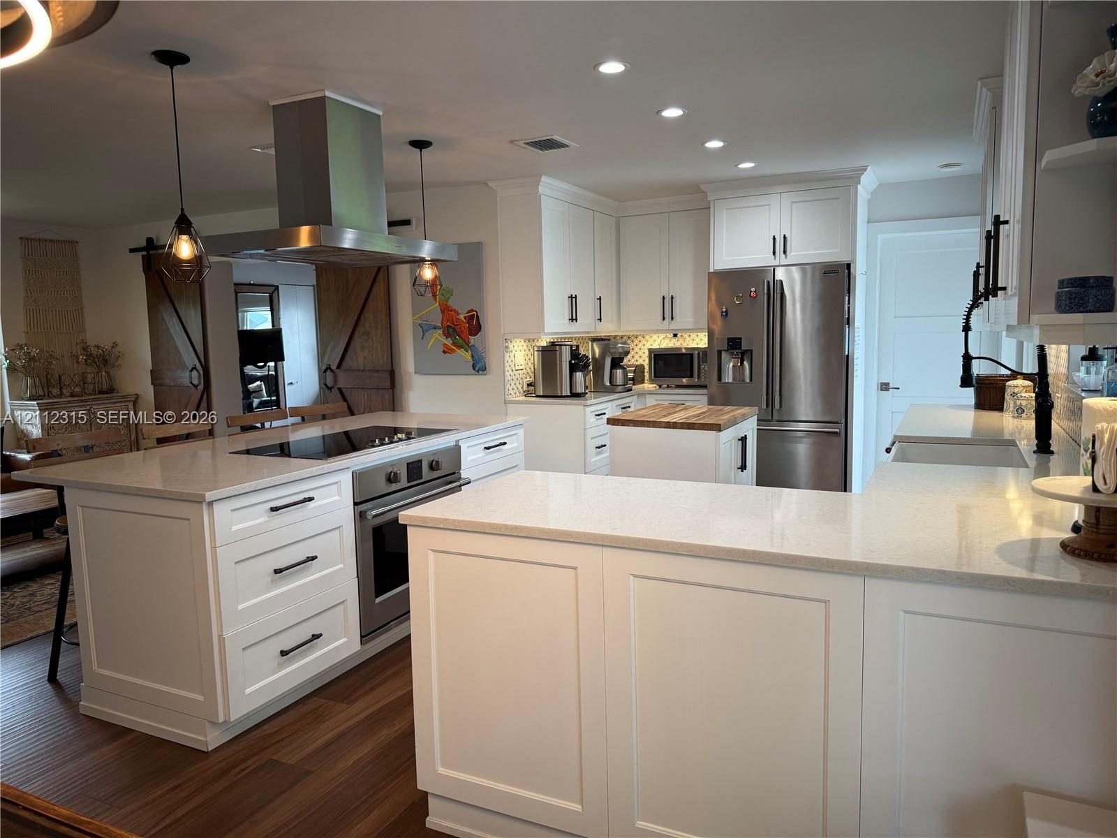 Kitchen featuring white shaker-style cabinetry, quartz countertops, a central island with a built-in range, stainless steel appliances, and wood-finish flooring