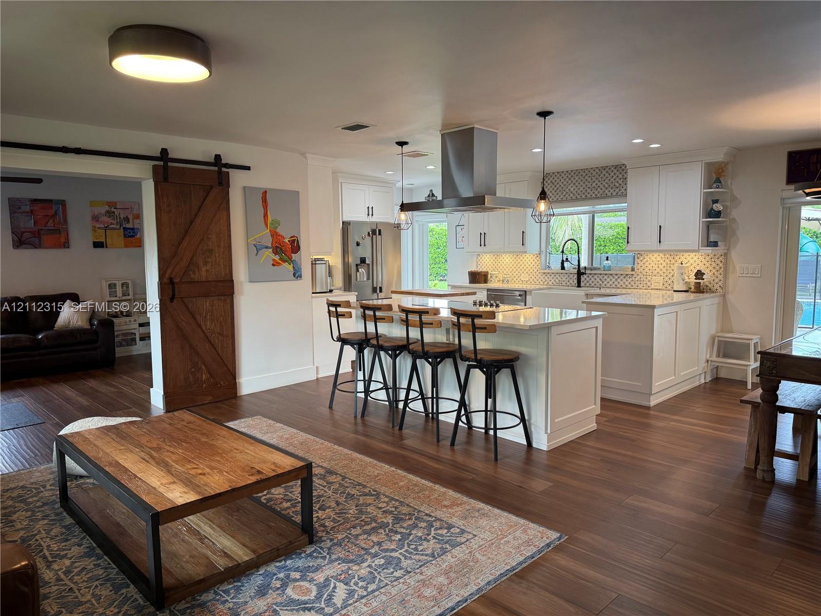 Kitchen featuring white shaker-style cabinetry, a central island with countertop seating, stainless steel appliances, a geometric-pattern backsplash, and wood-finish flooring