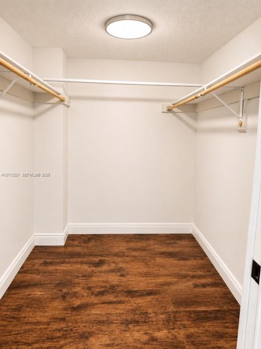 Walk-in closet featuring wood-finish flooring, dual-level white metal hanging rods, and a circular flush-mount ceiling light