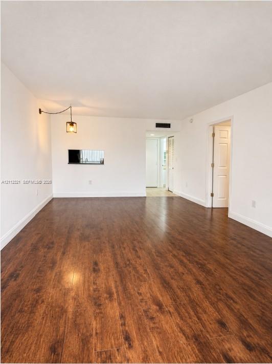 Interior space featuring dark wood-finish flooring, a wall-mounted industrial-style pendant light, and a pass-through opening Interior space featuring dark wood-finish flooring, a wall-mounted industrial-style pendant light, and a pass-through opening