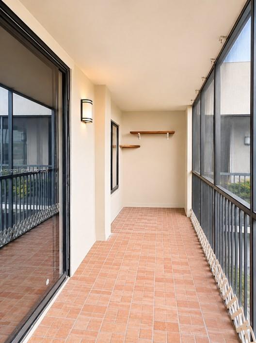Covered balcony featuring terracotta-style tile flooring, floor-to-ceiling screened enclosures, metal railings, wall-mounted exterior lighting, and built-in wood shelving Covered balcony featuring terracotta-style tile flooring, floor-to-ceiling screened enclosures, metal railings, wall-mounted exterior lighting, and built-in wood shelving