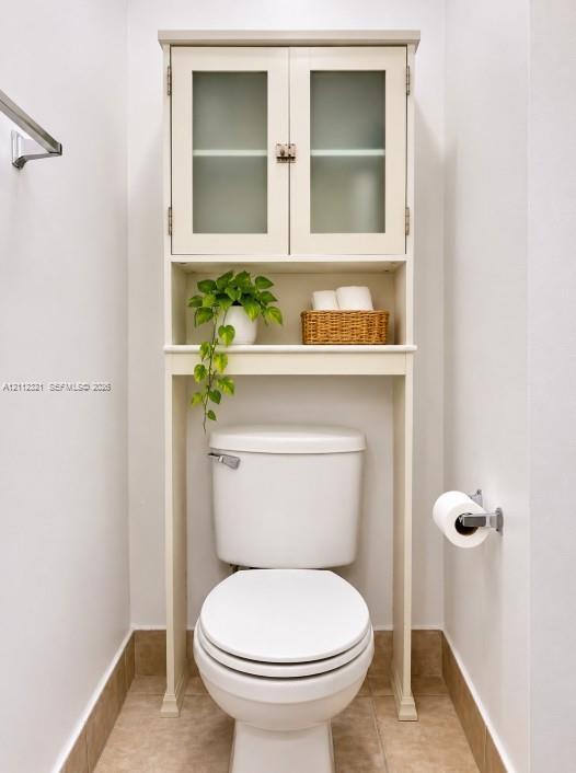 Built-in cabinetry featuring glass-panel doors and open shelving, paired with a ceramic toilet, stainless steel towel bar, and metallic toilet paper holder