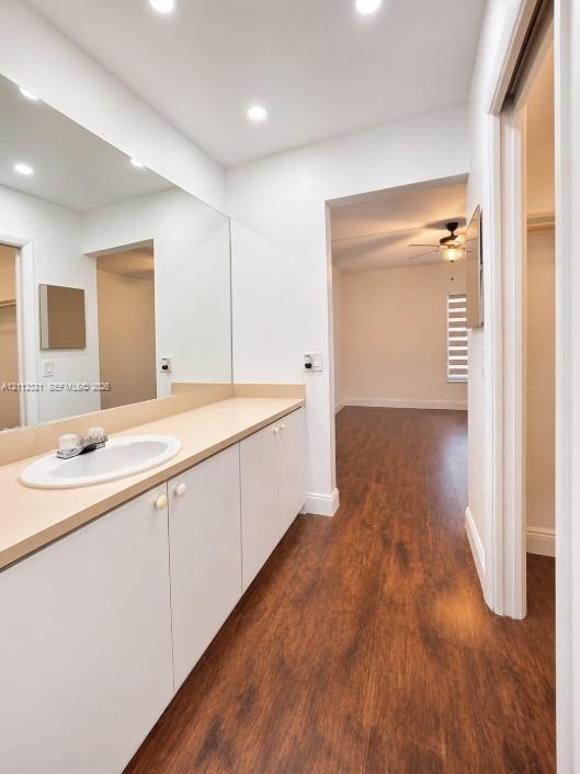 Bathroom vanity featuring white cabinetry, a solid surface countertop, an undermount oval sink, and a full-width wall mirror, complemented by wood-finish flooring