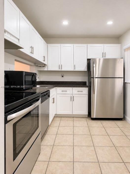 Kitchen featuring white Shaker-style cabinetry, dark stone-finish countertops, stainless steel appliances, and ceramic tile flooring