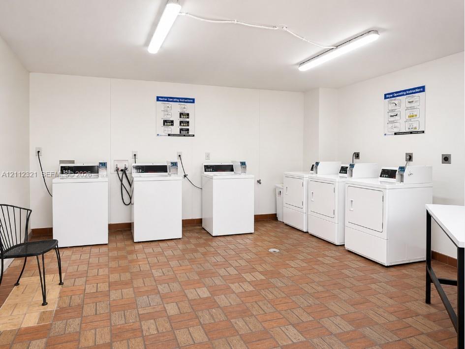 Laundry area featuring multiple coin-operated washing machines and dryers with ceramic tile flooring and linear fluorescent lighting