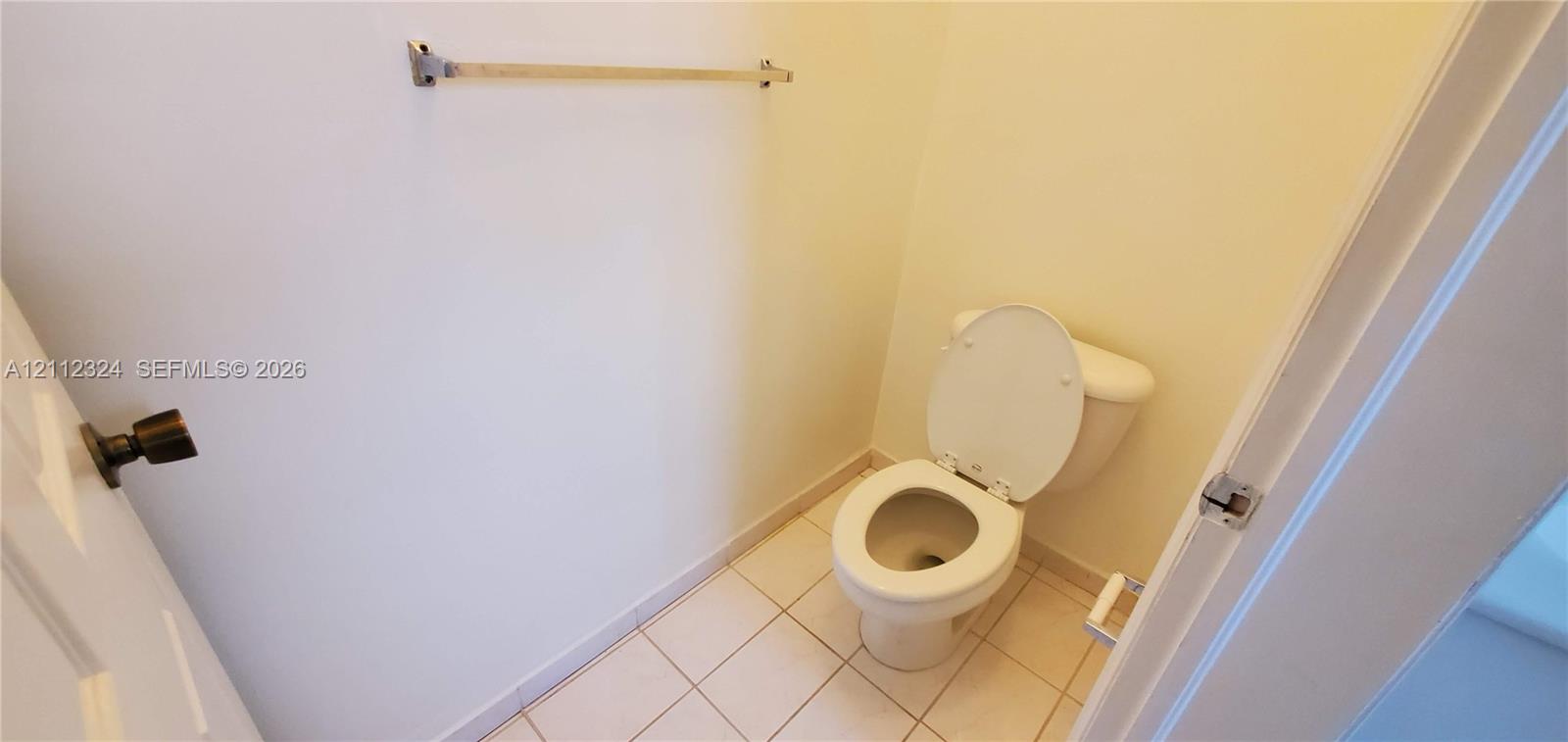 Restroom featuring white ceramic tile flooring, a porcelain toilet, and a mounted metal towel bar