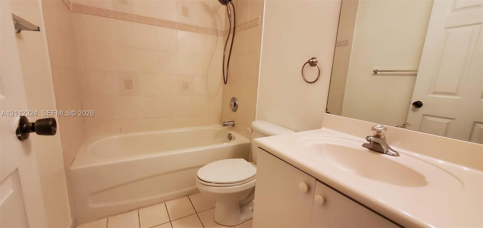 Bathroom featuring a white molded vanity with an integrated basin, wall-mounted mirror, ceramic tile flooring, and a shower-tub combination with tiled surround
