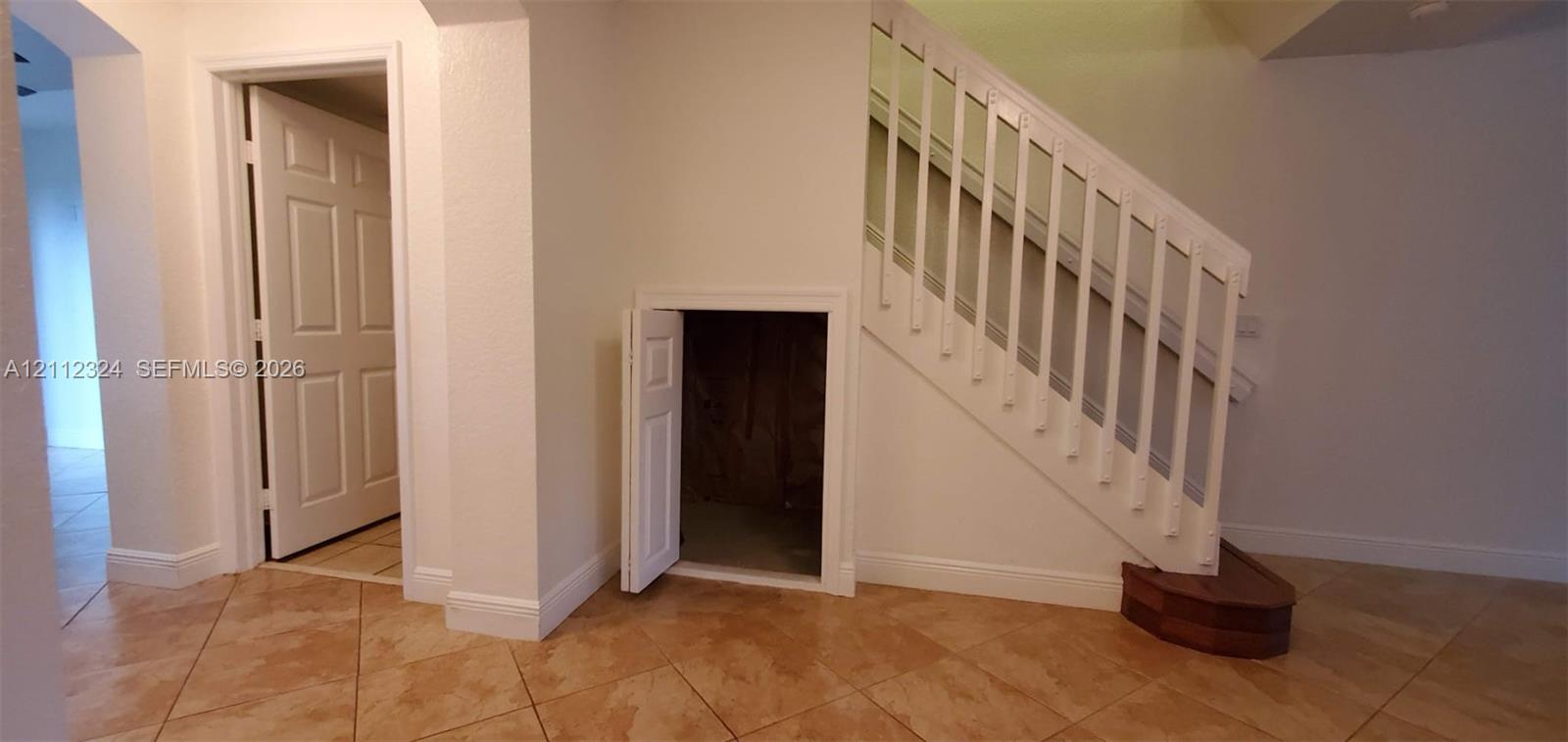 Interior area featuring ceramic tile flooring, a staircase with a white wood-finish balustrade, and a built-in under-stair storage compartment with a solid panel door