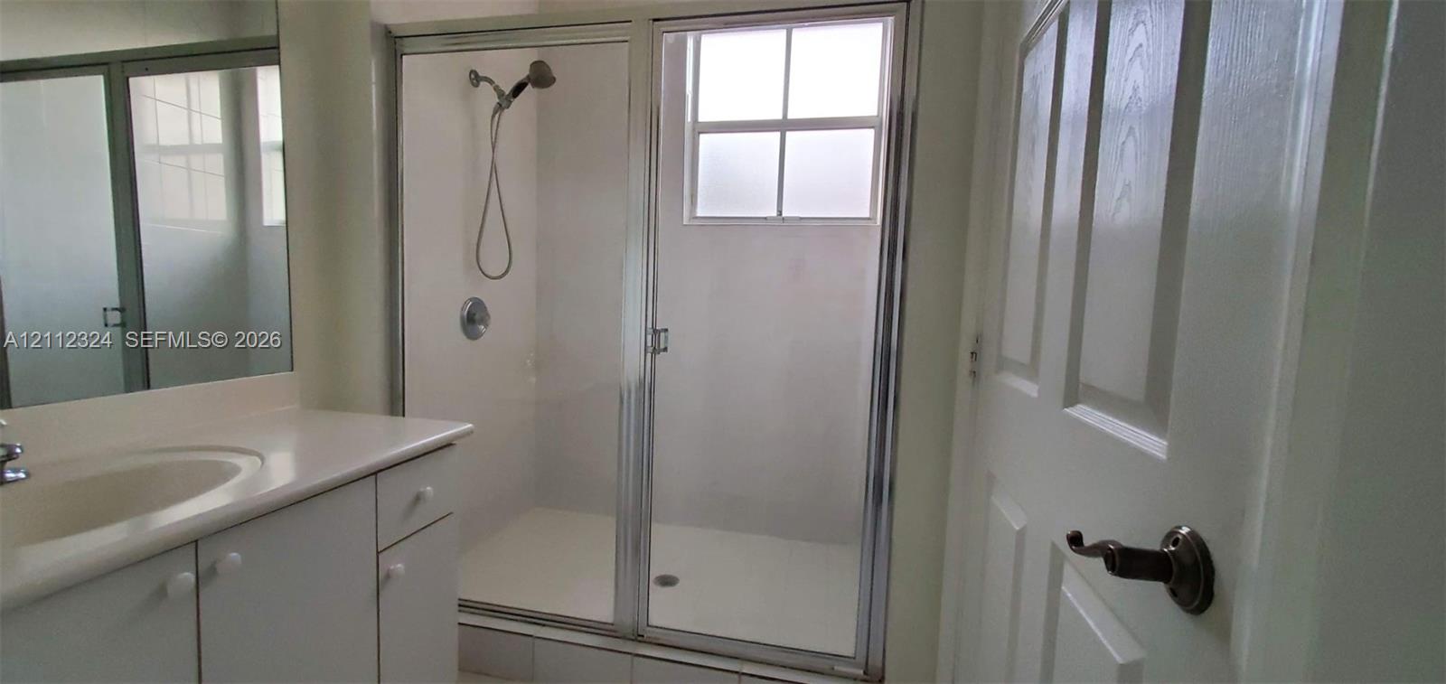 Bathroom featuring a vanity with a solid-surface countertop, an integrated sink, a glass-enclosed shower with a handheld fixture, and a window for natural light