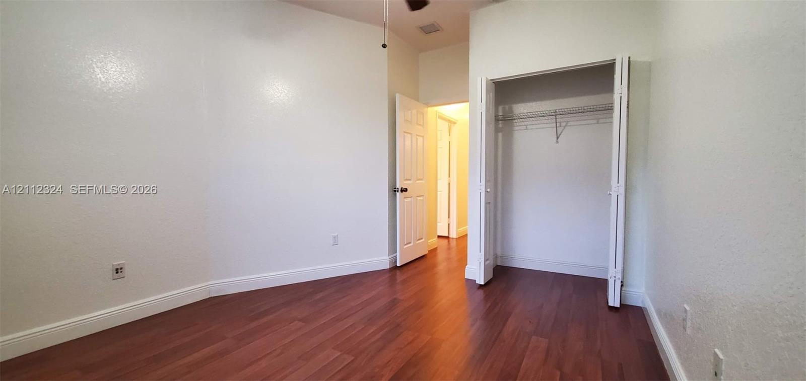 Room featuring wood-finish flooring, textured walls, a ceiling fan, and a built-in closet with wire shelving