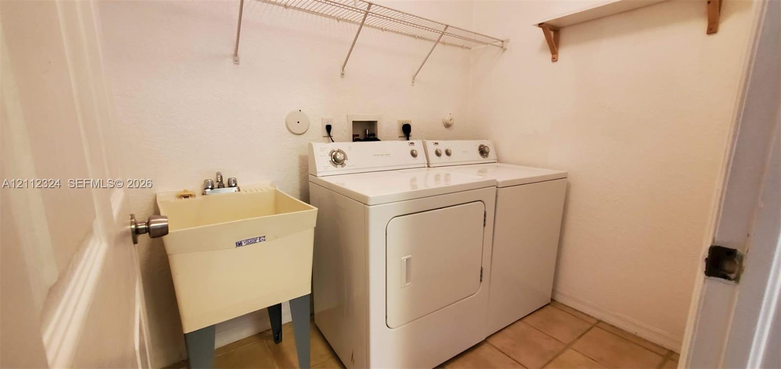 Laundry area featuring a utility sink, metal wall-mounted shelving, and tile flooring