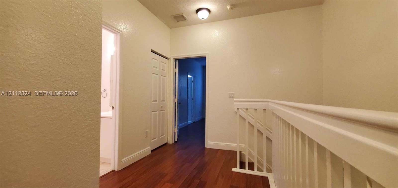 Hallway featuring wood-finish flooring, white paneled doors, and a white balustrade with a matching handrail