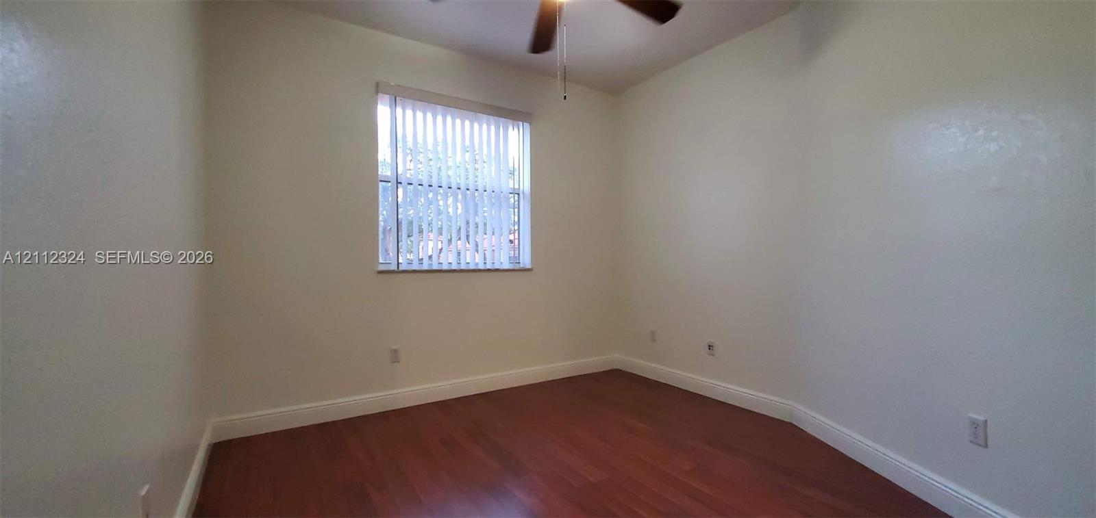 Neutral-toned room featuring wood-finish flooring, a single-pane window with vertical blinds, and a ceiling fan