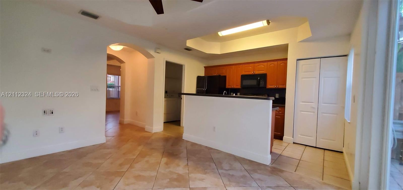 Kitchen featuring a peninsula counter, wood-finish cabinetry, built-in microwave, tiled flooring, and a tray ceiling with recessed lighting
