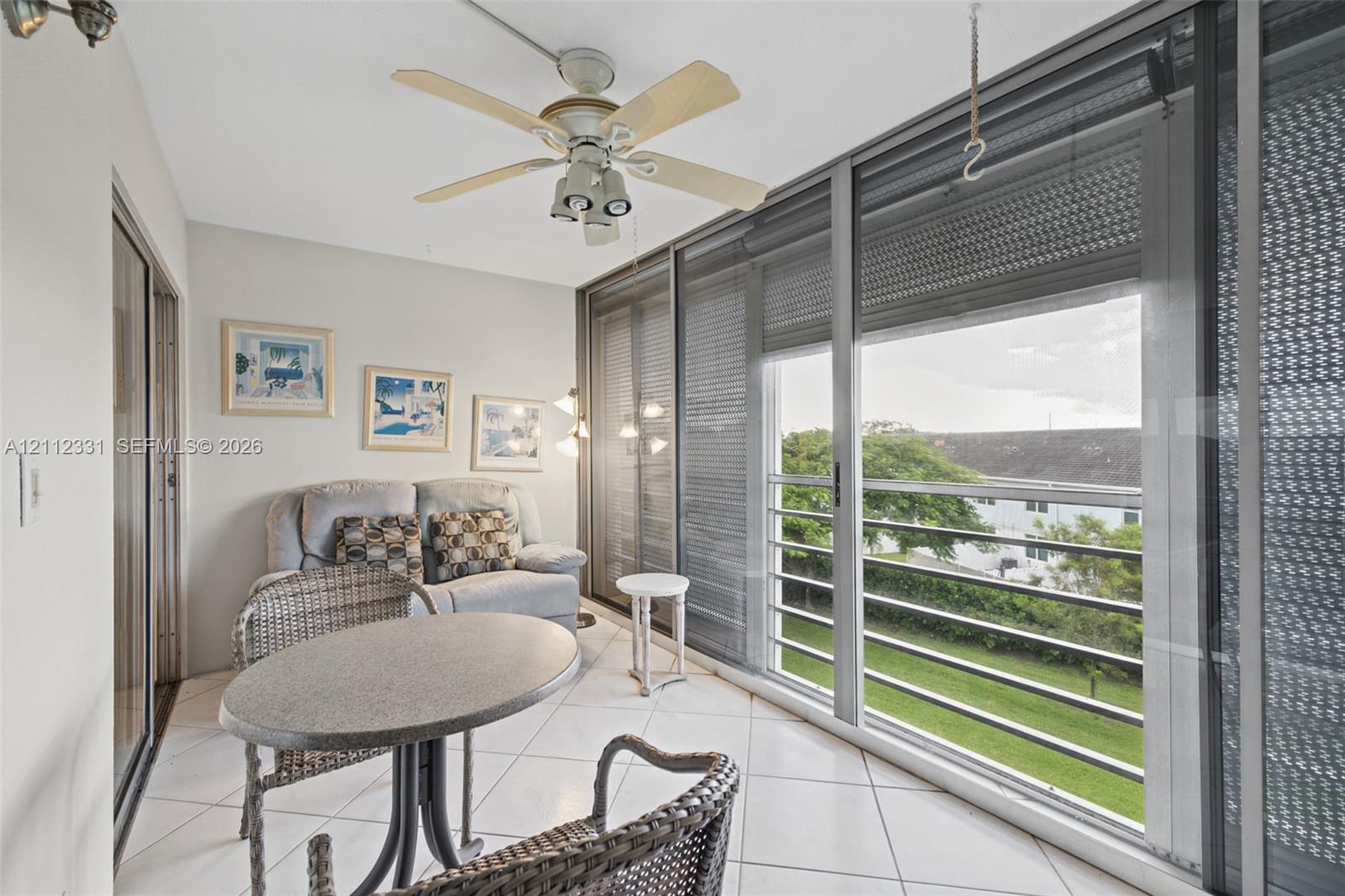 Enclosed balcony featuring large-format ceramic tile flooring, a white ceiling fan with integrated lighting, and expansive floor-to-ceiling sliding glass doors with horizontal blinds