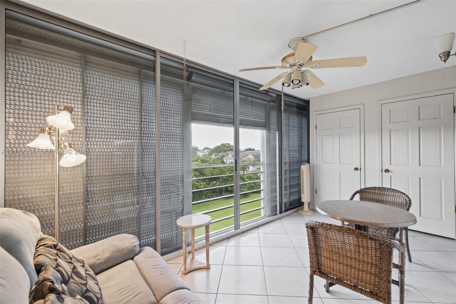 Enclosed sunroom featuring light-colored ceramic tile flooring, floor-to-ceiling sliding glass doors, a ceiling fan with integrated lighting, and two interior six-panel doors