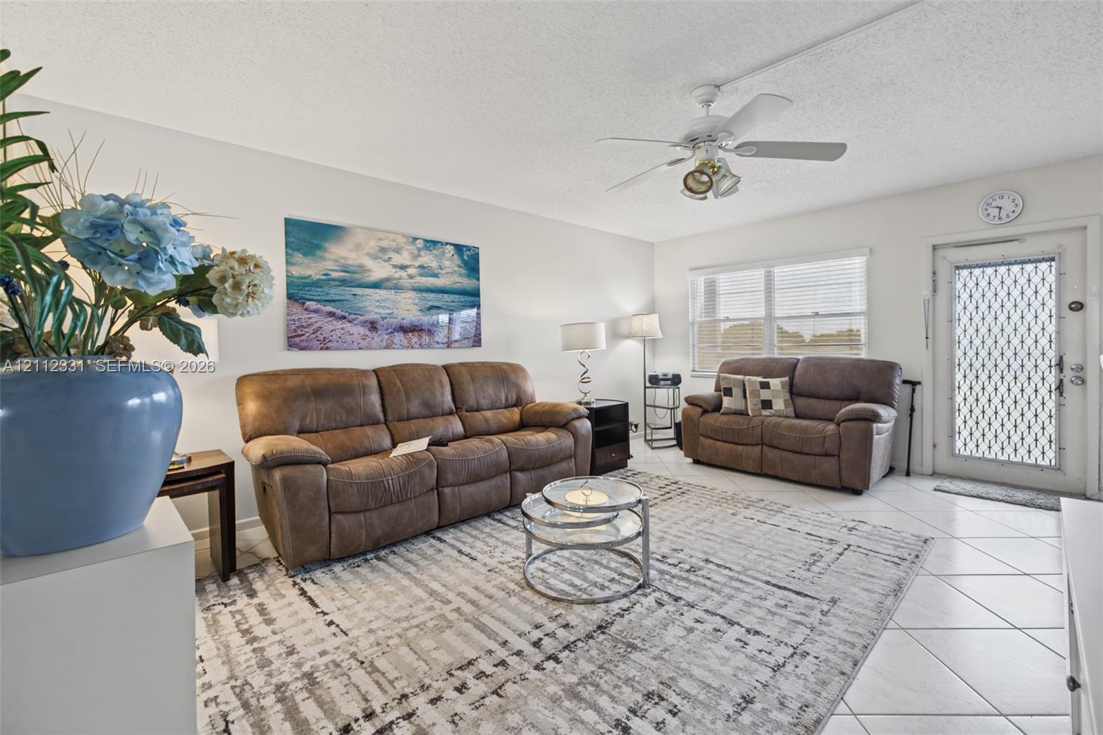 Living area featuring neutral-toned tile flooring, a multi-blade ceiling fan with integrated lighting, and a security-screen entry door