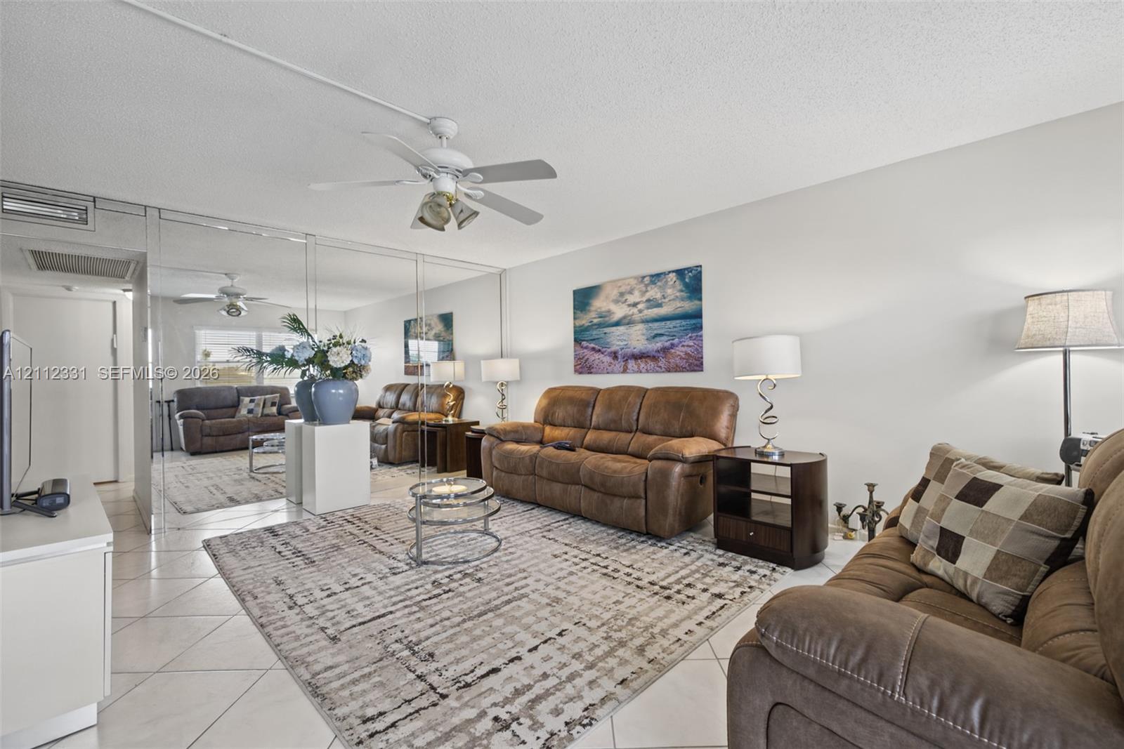 Living area featuring neutral tile flooring, mirrored wall paneling, and a ceiling-mounted light fixture with fan