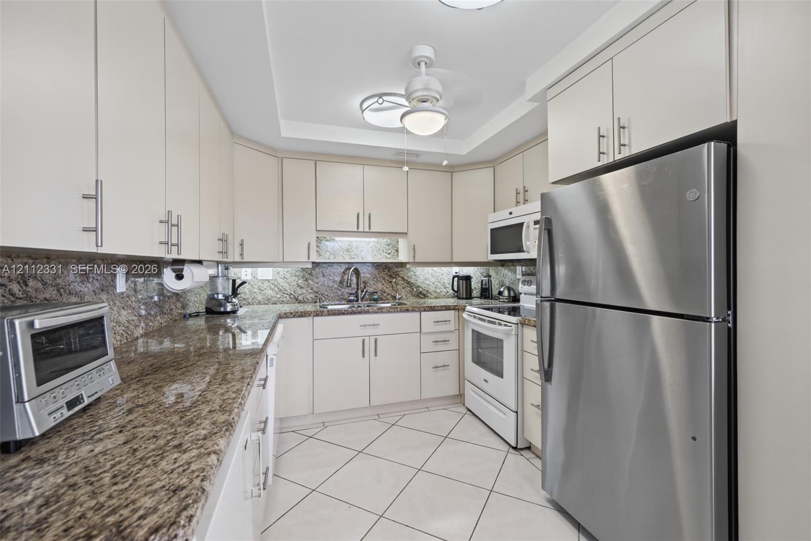 Kitchen featuring white cabinetry, stone-patterned countertops, stainless steel appliances, and tiled flooring