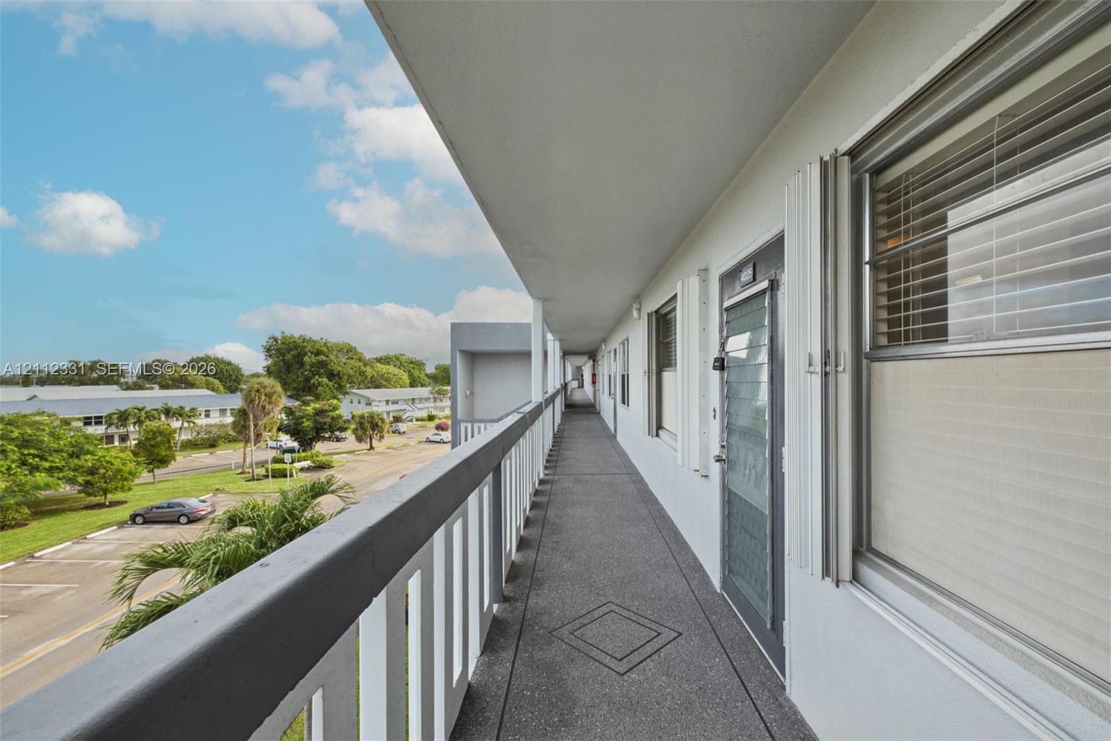 Covered exterior walkway featuring a textured concrete floor, metal railings, and integrated security door screening