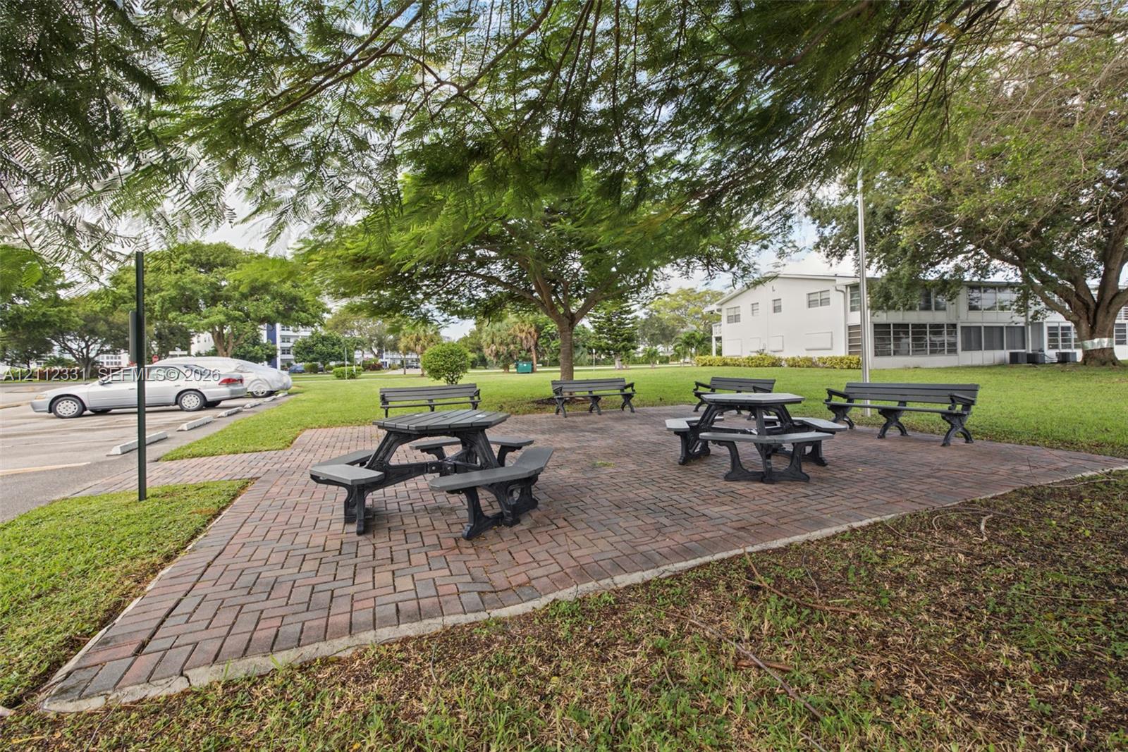 Outdoor common area featuring a brick-paver patio, permanent benches, and mature shade trees