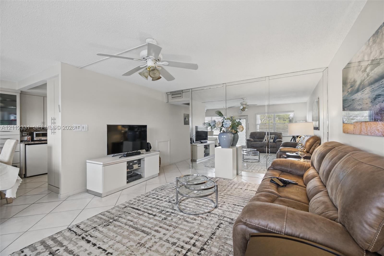 Open-concept interior featuring large-format diagonal tile flooring, a ceiling fan with integrated lighting, and a full-wall mirrored accent