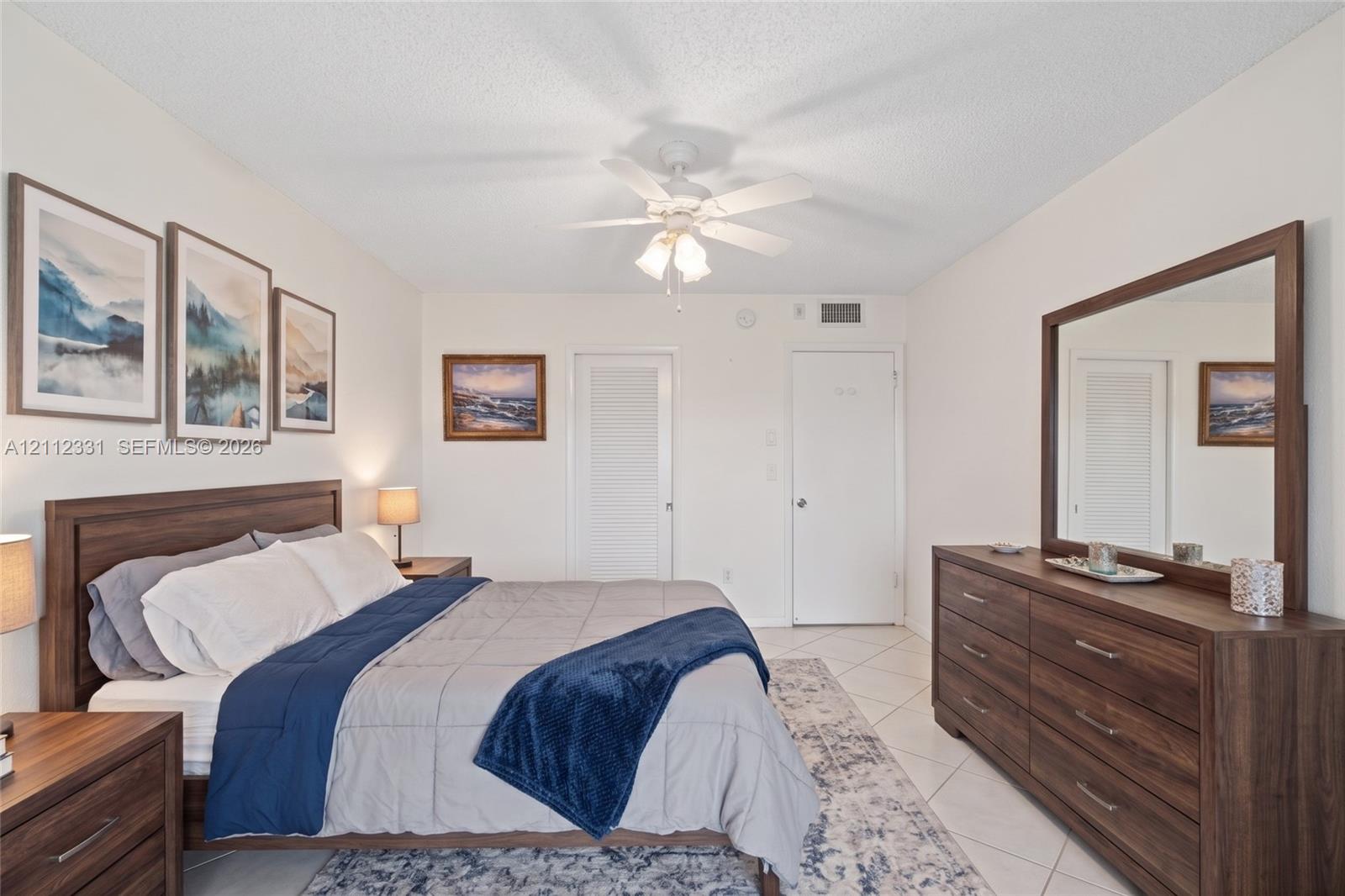 Bedroom featuring white walls, white tile flooring, and a white ceiling fan with integrated lighting