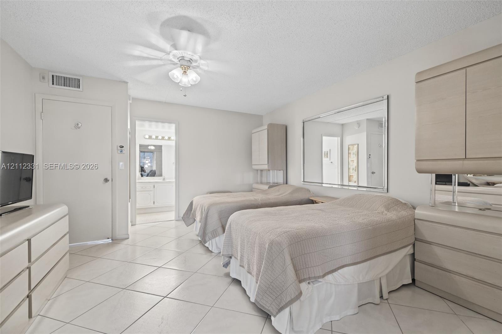 Neutral-toned space featuring large-format diagonal tile flooring, custom built-in light-wood cabinetry, a wall-mounted glass mirror, and a central ceiling fan with integrated lighting