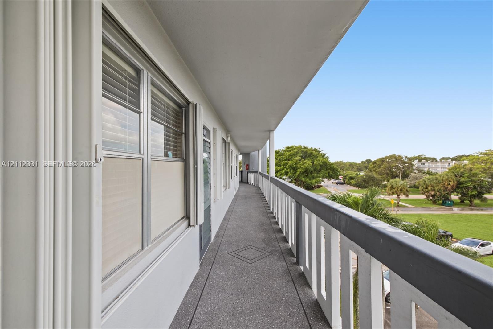 Covered exterior walkway featuring a textured concrete surface, metal railing, and recessed wall-mounted lighting