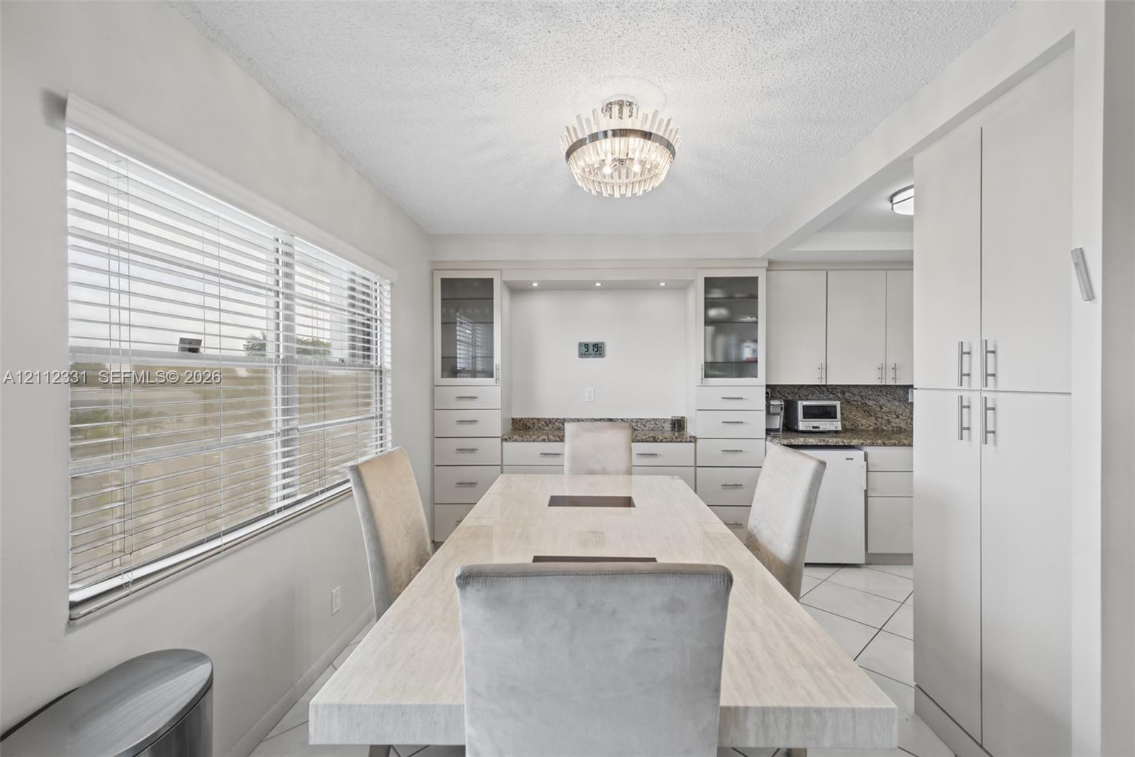 Built-in cabinetry with integrated shelving and drawers, stone-finish countertops, tile flooring, large horizontal window with blinds, and decorative chandelier lighting